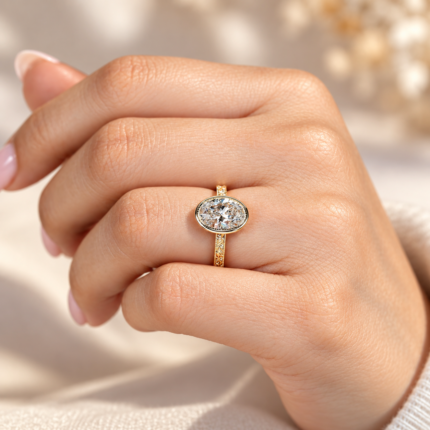 Oval bezel diamond ring worn on curled fingers, showing the milgrain border and engraved gold tone band