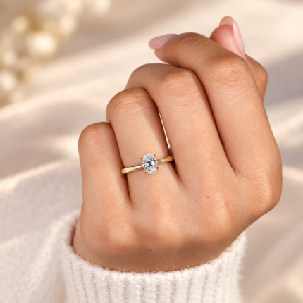 Oval cathedral solitaire diamond ring on a curled hand, showing the tapered gold tone shoulders
