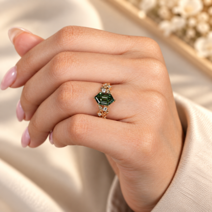 Green hexagon diamond ring worn on a curled hand, showing the botanical gold tone band and step cut center