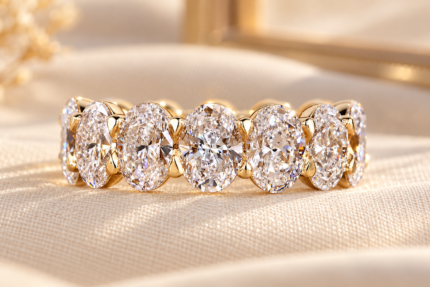 Close-up of oval lab diamond shared prong eternity band on cream fabric