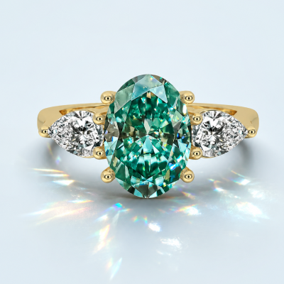 Gold three-stone ring with an oval green center stone and pear-shaped side stones